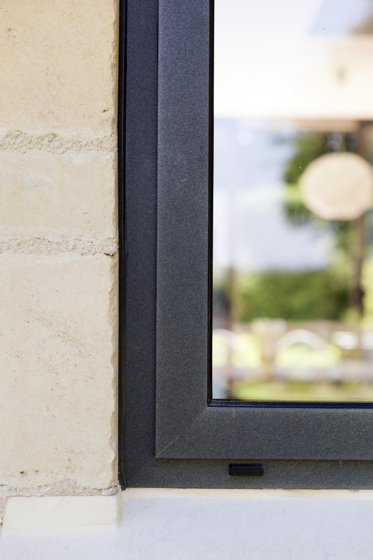 Close-up detail of an anthracite grey aluminium window frame against a stone wall