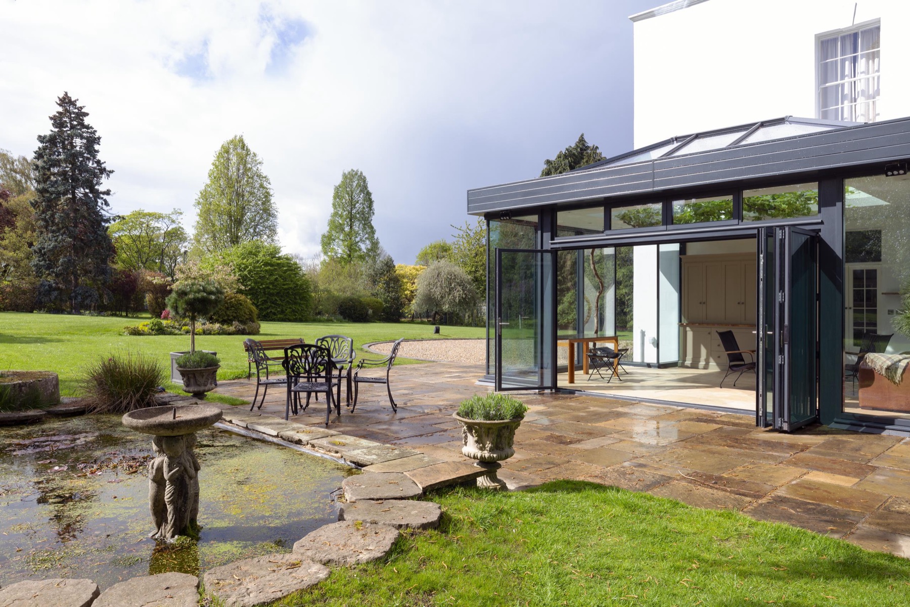 An anthracite grey aluminium bifold door fully open between a garden room and a landscaped garden